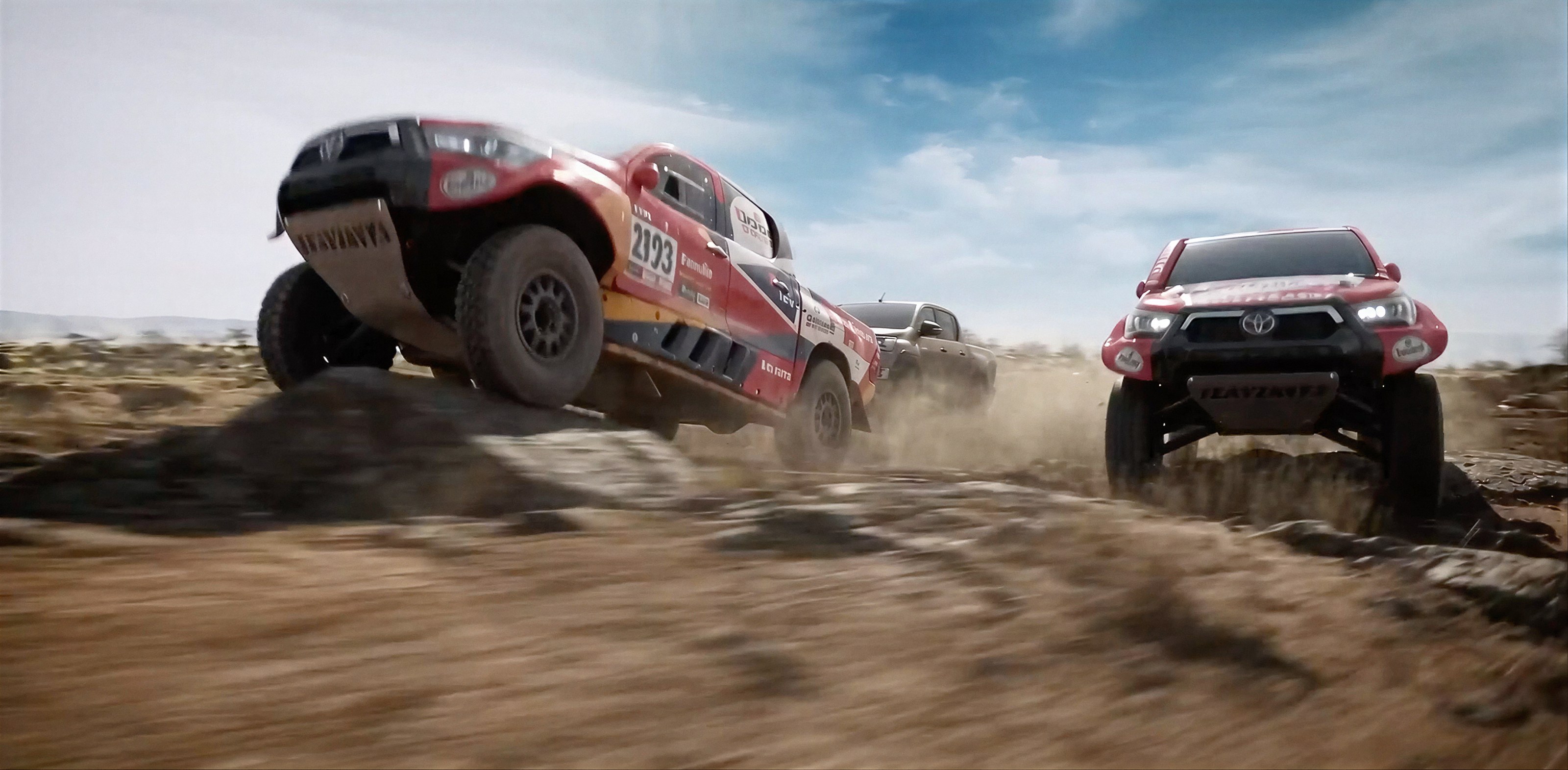 Toyota Gazoo Racing Hilux rally trucks leaping over rocks in a dusty African landscape